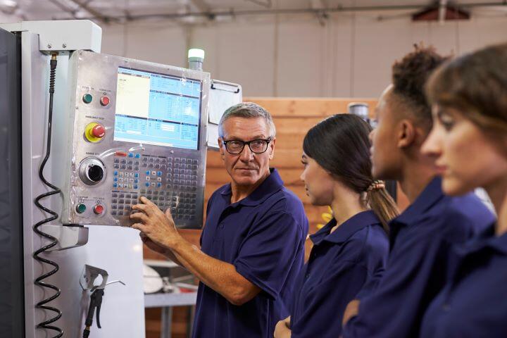 Ingenieur, der Lehrlinge an einer CNC-Maschine ausbildet, verkleinert für die Webseite